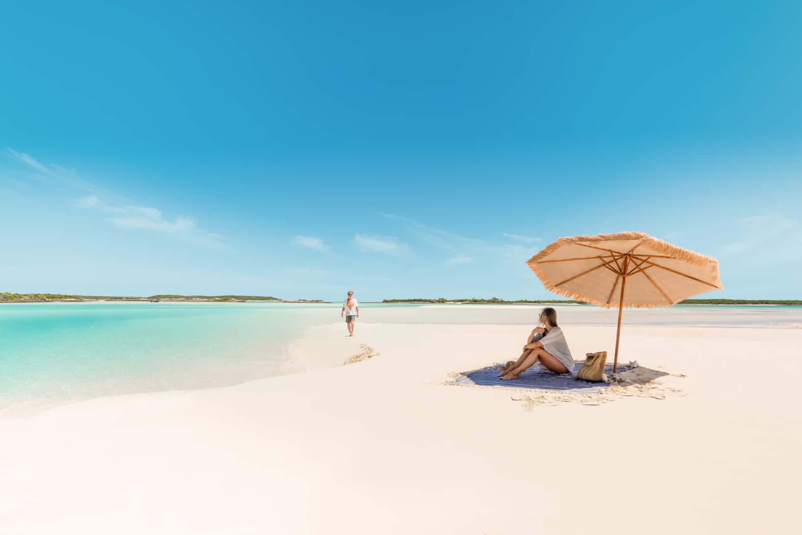 Two people sitting under an umbrella on a Staniel Cay beach.
