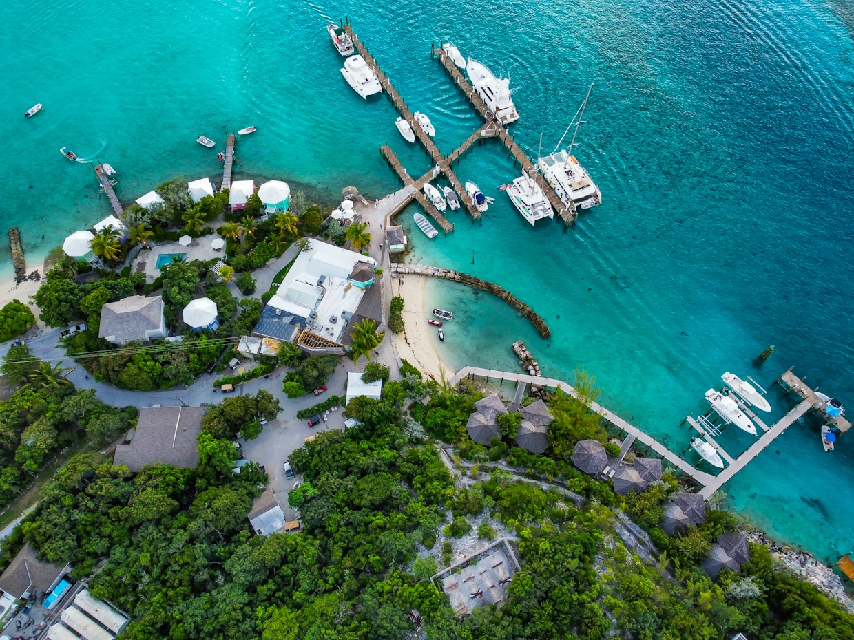 Staniel Cay Yacht Club Aerial view of a tropical marina near Staniel Cay Resort, with several boats docked at piers, surrounded by turquoise water and lush greenery. Vacation Rentals and Resort on Staniel Cay Exuma