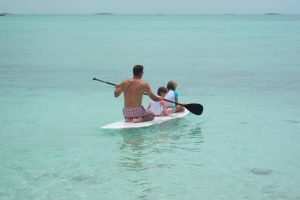 A family on a paddle board in the clear blue water of Staniel Cay, Bahamas.