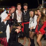 A group of people in pirate costumes posing for a photo at Staniel Cay, with Staniel Cay Yacht Club in the background.