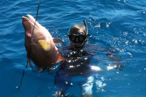 A man in a snogging suit holding a large fish while enjoying his vacation at Staniel Cay Yacht Club in The Bahamas.