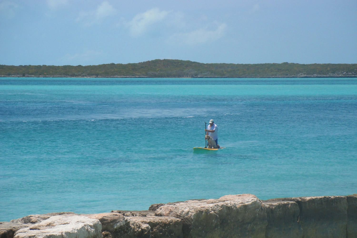 A man is riding a paddle board in the crystal clear waters of Staniel Cay.