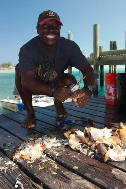 A man squatting on a dock with a bunch of shells in Staniel Cay, The Bahamas.