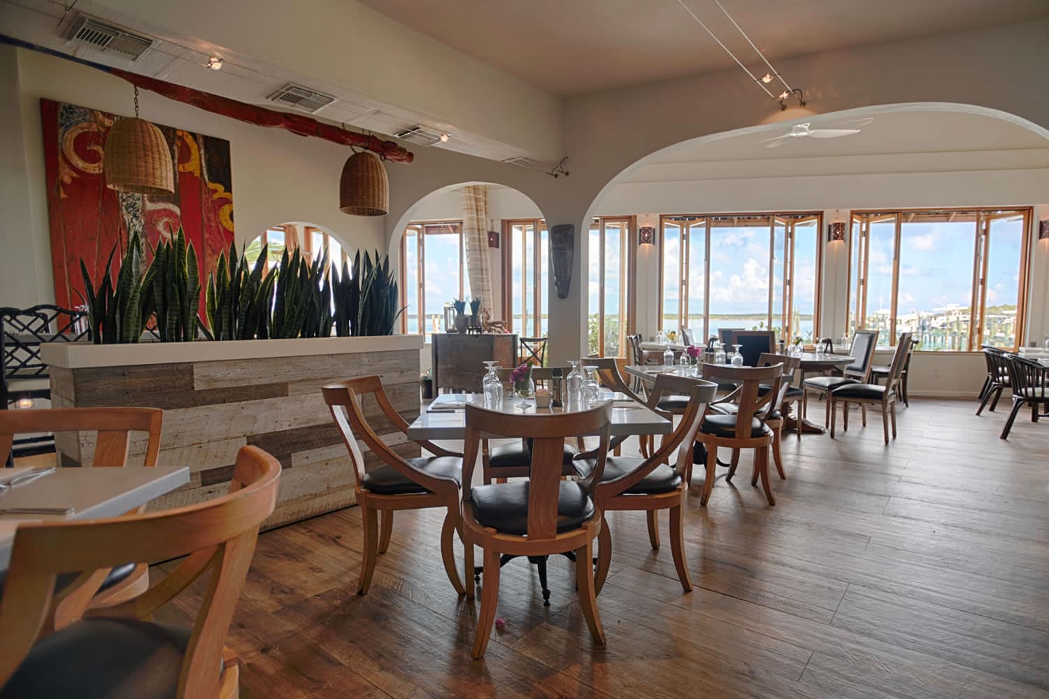 A restaurant with wooden tables and chairs and a view of the ocean, located on Staniel Cay in The Bahamas.