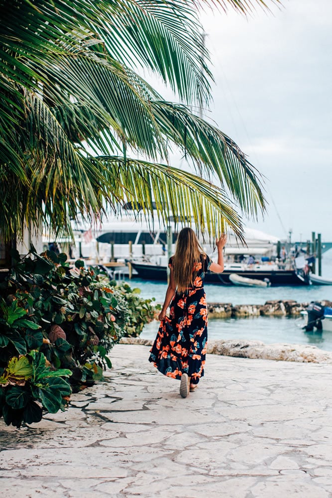 A woman in a floral dress walking down a path near a boat in Staniel Cay, The Bahamas.