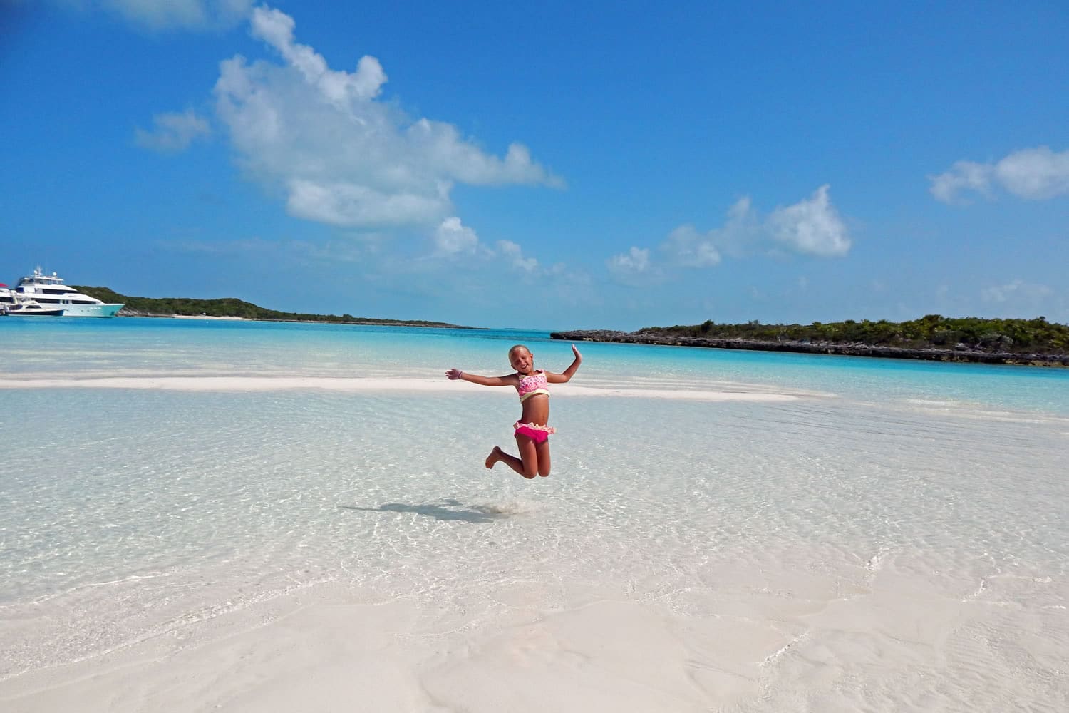A woman jumping in the air on a white sandy beach in Staniel Cay.