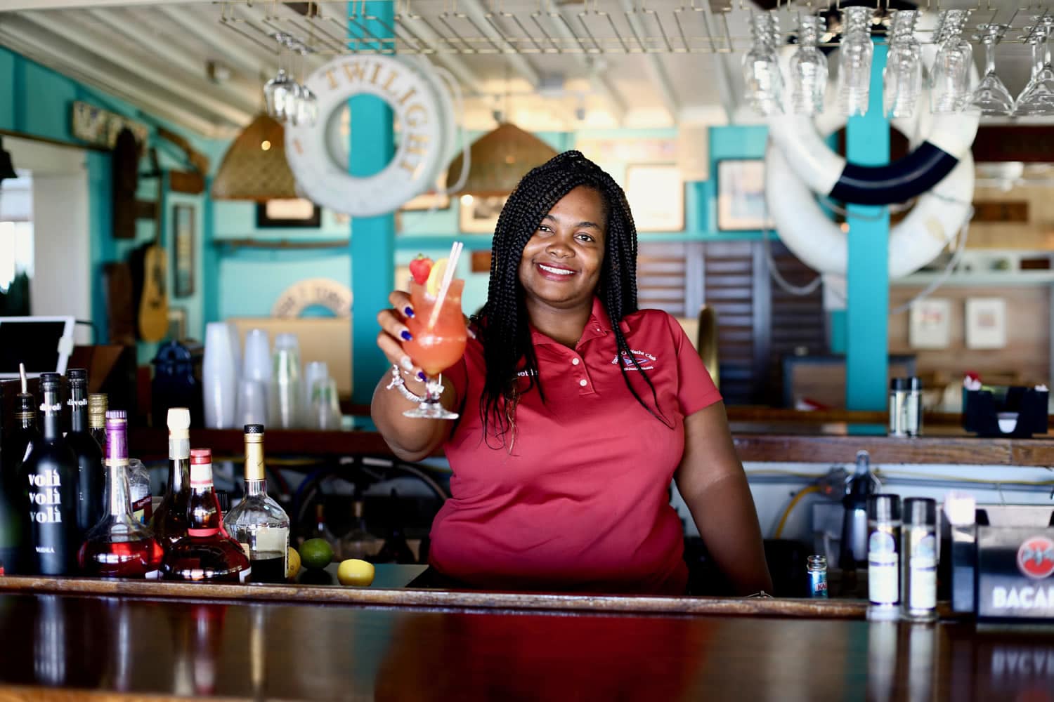 A woman standing behind a bar with a drink in her hand at Staniel Cay, The Bahamas.