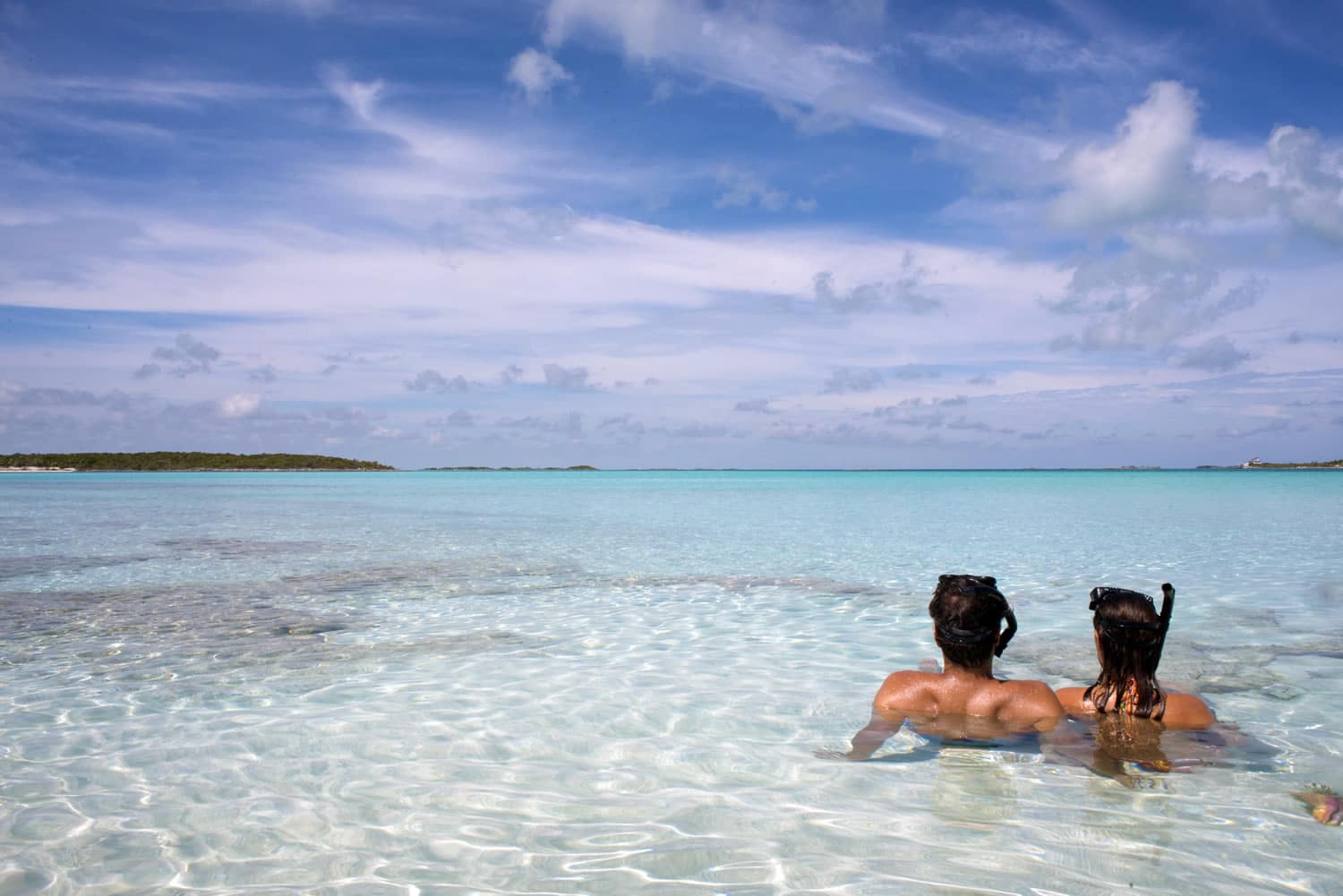 Two people enjoying a relaxing swim in the crystal-clear waters of The Bahamas.