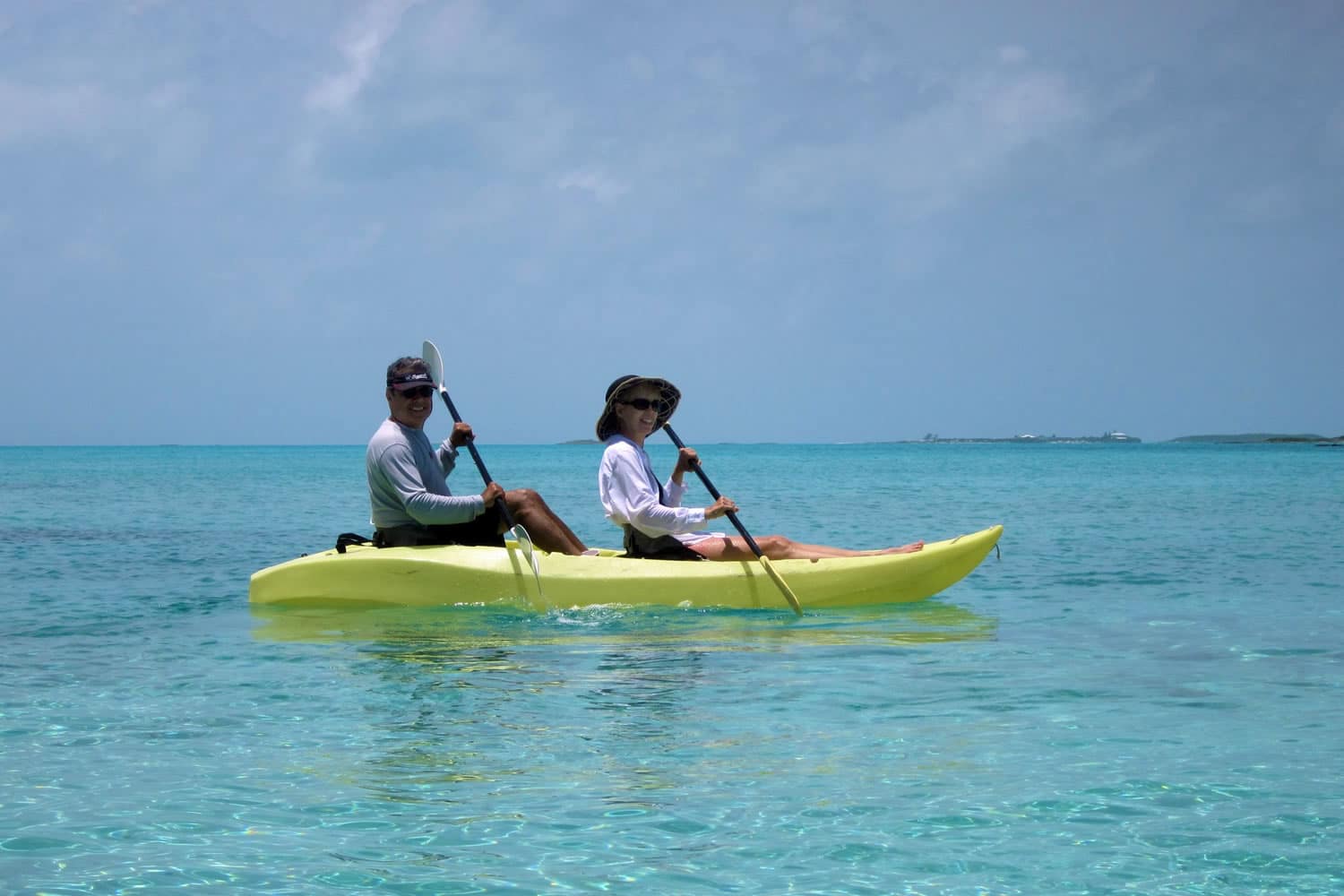 Two people paddling a yellow kayak in the clear blue water near Staniel Cay in The Bahamas.