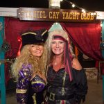 Two women in pirate costumes standing in front of a Staniel Cay yacht club tent.