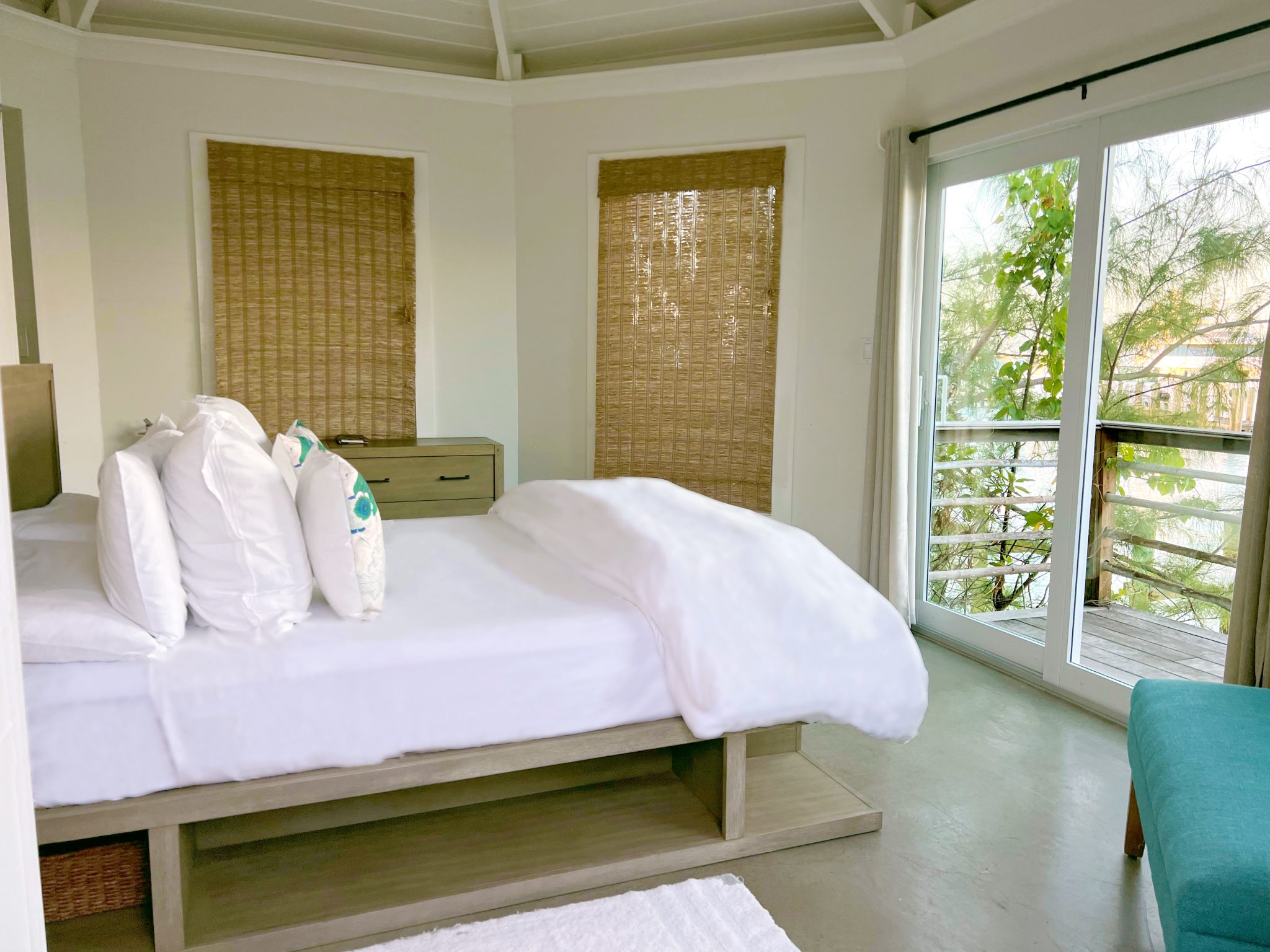 A bedroom in a Staniel Cay vacation rental with a white bed and a balcony overlooking the Staniel Cay Yacht Club.