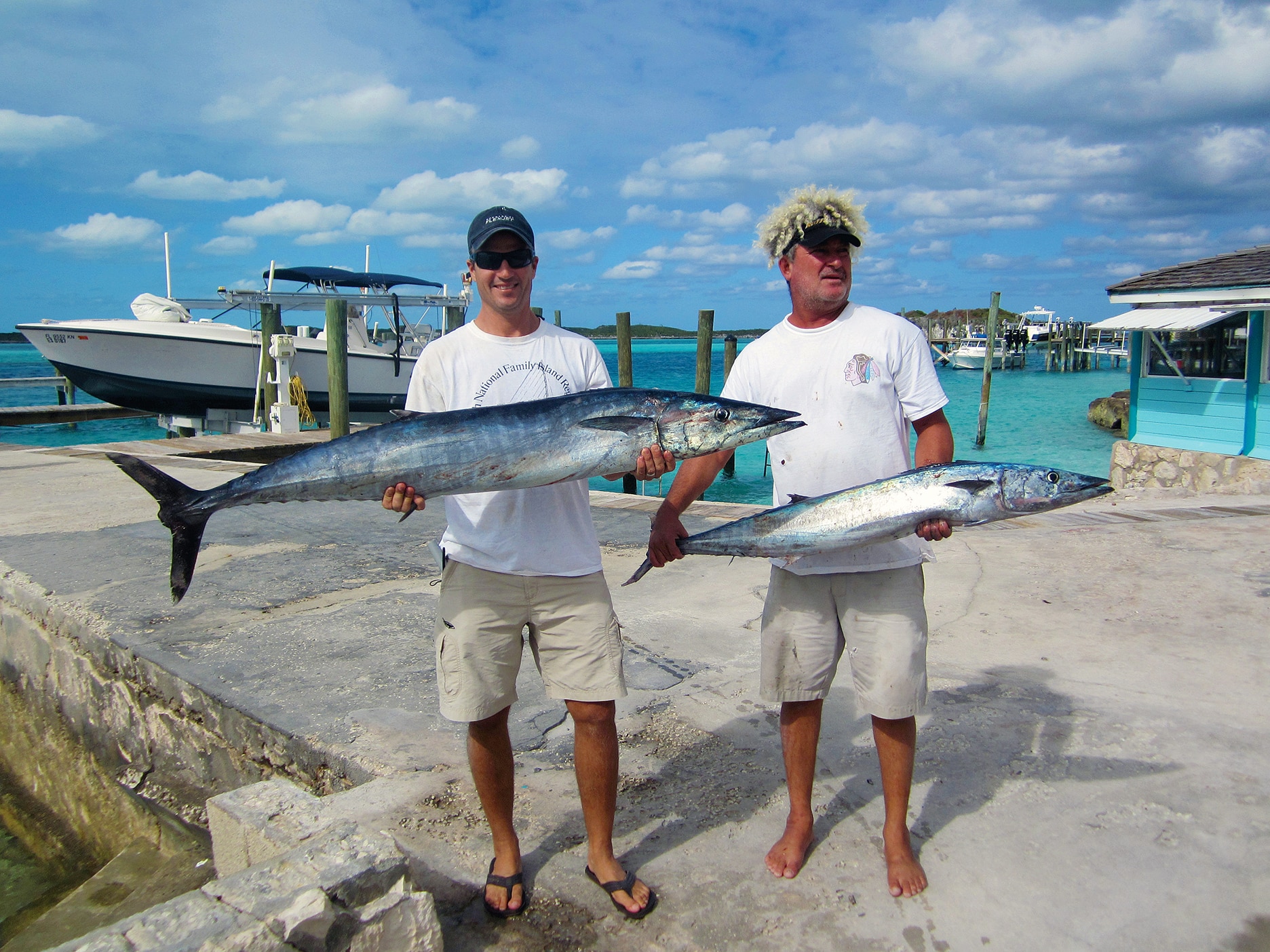 Two men holding fish in front of a Staniel Cay boat.