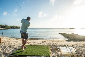 A man is hitting a golf ball at Staniel Cay Yacht Club on the beach.
