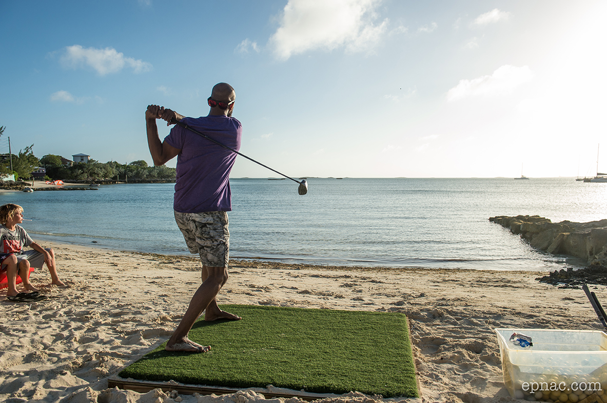 A man is playing golf at the Staniel Cay Yacht Club on the beach.