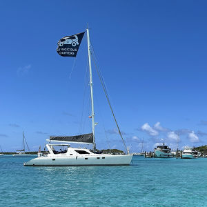 Staniel Cay Yacht Club A white sailing yacht with the "Magic Bus Charters" flag flutters in the breeze, anchored gracefully in clear blue waters. Other boats dot the background under a quintessential sunny sky, perfect for those seeking an idyllic yacht charter experience. Vacation Rentals and Resort on Staniel Cay Exuma