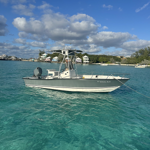 Staniel Cay Yacht Club A small motorboat floats on clear turquoise water, anchored near a shoreline with trees and several vacation rentals under a partly cloudy sky. Vacation Rentals and Resort on Staniel Cay Exuma