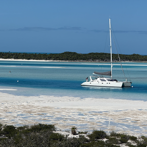 Staniel Cay Yacht Club A sleek white sailboat charter anchored in clear turquoise waters near a sandy beach offers the perfect getaway, framed by lush green vegetation and a vibrant blue sky. Vacation Rentals and Resort on Staniel Cay Exuma