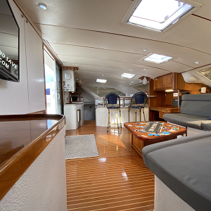 Staniel Cay Yacht Club The interior of a yacht charter features a wooden floor, a seating area with gray cushions, a table set for games, and a small kitchen with bar stools—an ideal setting for vacation rentals. Vacation Rentals and Resort on Staniel Cay Exuma